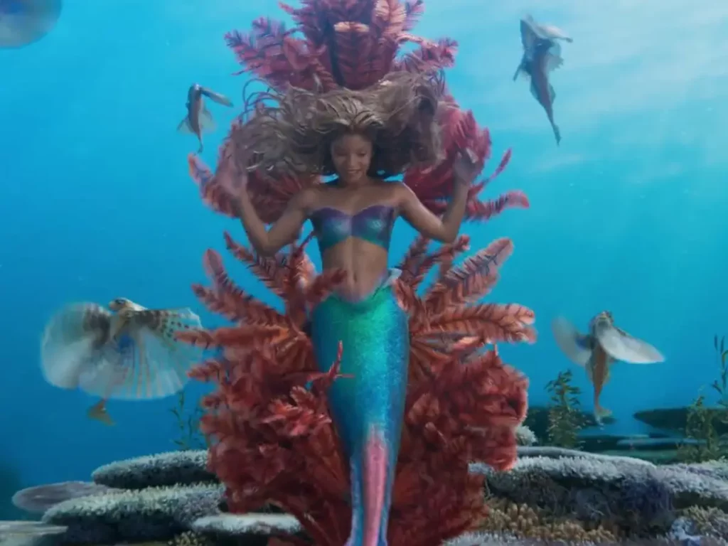 Halle Bailey as Ariel in an underwater scene with coral and fish from The Little Mermaid.