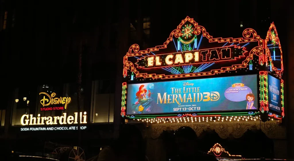 The El Capitan theater lit up at night with billboard for The Little Mermaid.