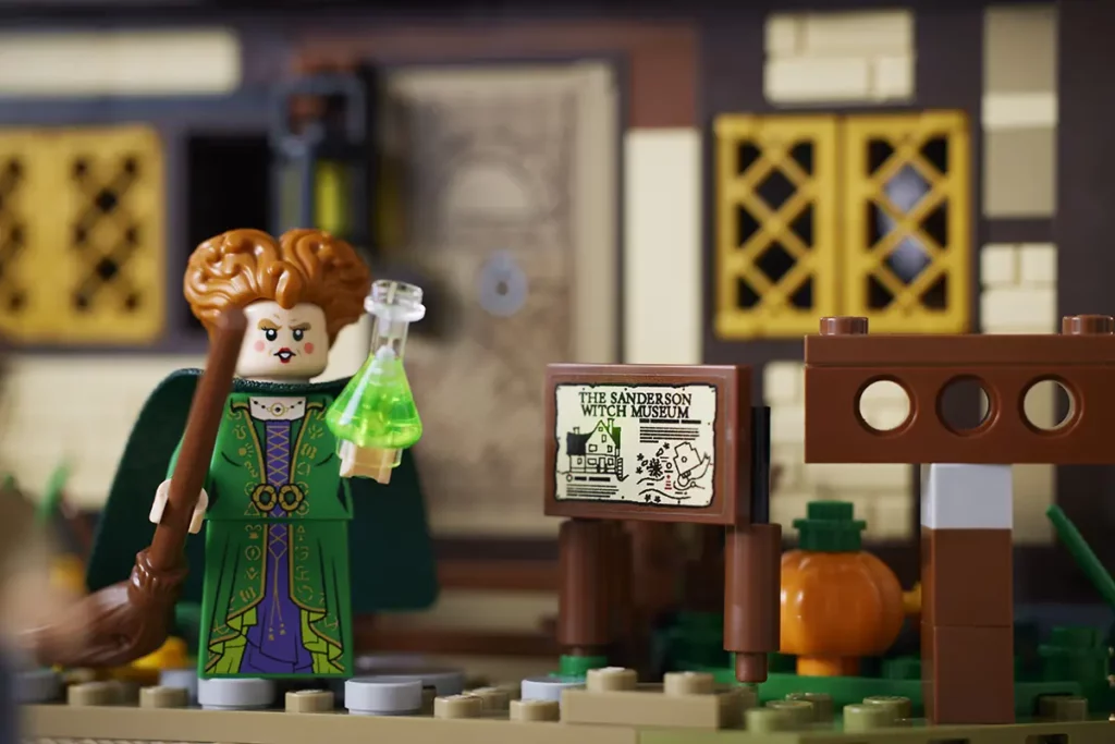 LEGO minifigure for Winifred Sanderson holding a green potion and standing in front of The Sanderson Witch Museum sign.